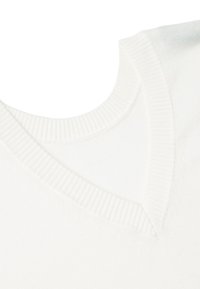 Vit stickad tröja med V-ringning, med ribbade detaljer längs kragen och axelsömmarna, slät textur och ren design.