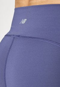 Leggings de sport violet taille haute avec une texture lisse, des coutures contrastées et un petit logo sur la taille.