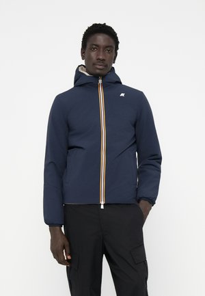Veste zippée bleu marine avec capuche, présentant des rayures verticales jaunes et blanches sur la fermeture éclair, et des poignets élastiques. Tissu léger.
