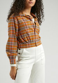 Cropped plaid jacket in orange, blue, and pink with button closure and elastic waistband; paired with white high-waisted pants featuring side buttons.