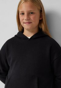 Zwarte hoodie gemaakt van zachte stof, met een kangoeroezak en een capuchon met trekkoord. Eenvoudig ontwerp zonder zichtbare patronen of accenten.
