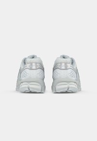 Um par de sapatilhas de corrida Nike cinza claro vistas de trás sobre um fundo branco liso.