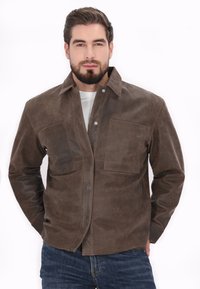 Veste en cuir marron avec un devant à boutons, deux grandes poches poitrine et un col plat. Texture lisse avec des accents de couture visibles.