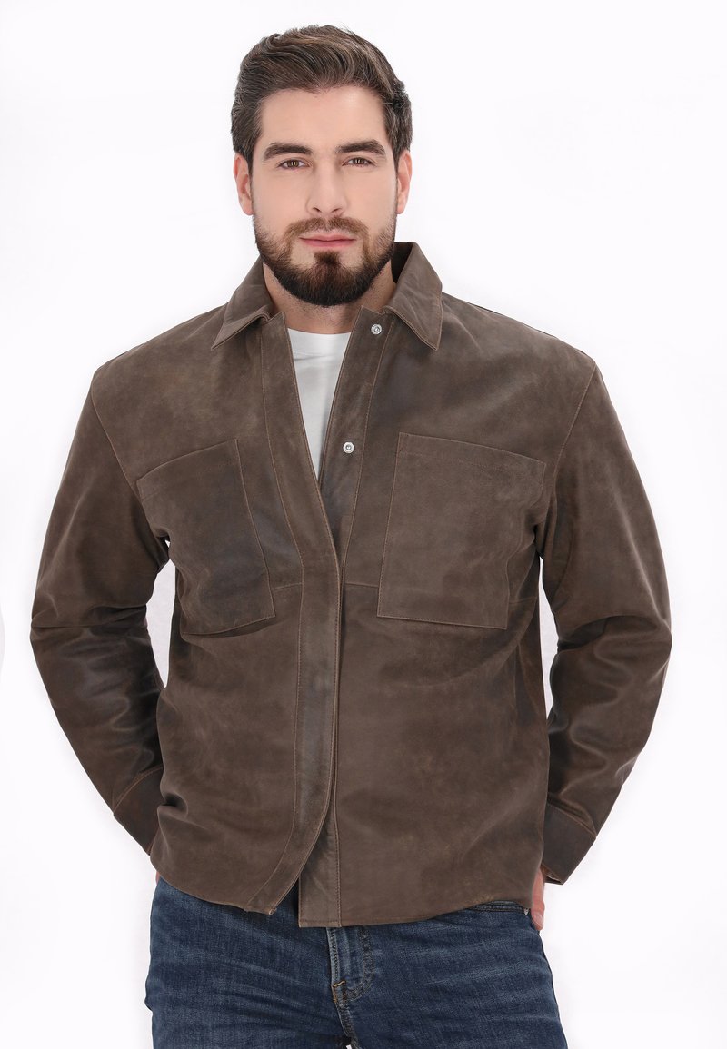 Veste en cuir marron avec un devant à boutons, deux grandes poches poitrine et un col plat. Texture lisse avec des accents de couture visibles.