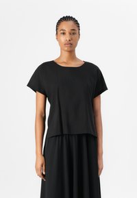 Haut noir à manches courtes avec un col arrondi, fabriqué en tissu léger, présentant une coupe ample et un design légèrement court.