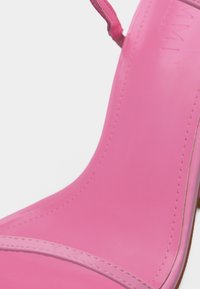 Κοντινή λήψη της σόλας και του λουριού στον αστράγαλο του ροζ σανδαλιού με ψηλό τακούνι, με ορατή ραφή και υφή από λείο δέρμα.