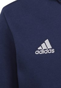 Tessuto blu navy con logo Adidas ricamato in bianco, che mostra tre strisce inclinate sopra il nome del marchio.