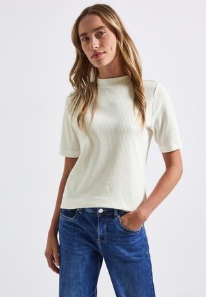 Haut blanc à manches courtes en maille côtelée avec un col montant, associé à un jean en denim bleu avec poches avant et coutures visibles.