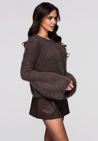 Suéter marrón de punto con mangas anchas y tela texturizada, combinado con pantalones cortos oscuros. Material suave y esponjoso con un patrón acanalado.