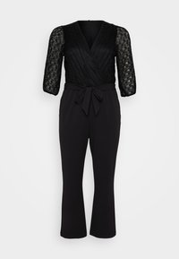 Svart jumpsuit med spetsliv, trekvartslånga ärmar, djup V-ringning, midja med bälte och raka byxor.
