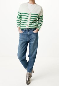 Cárdigan a rayas verdes y blancas con botones en el frente, usado sobre una camisa blanca, combinado con jeans de mezclilla azul claro y botines de tacón metálicos.