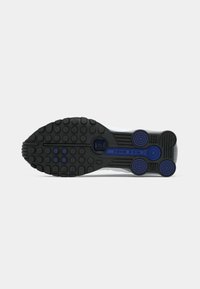 Black and blue rubber sole of a Nike Shox shoe with circular tread patterns and visible brand name on a white background.