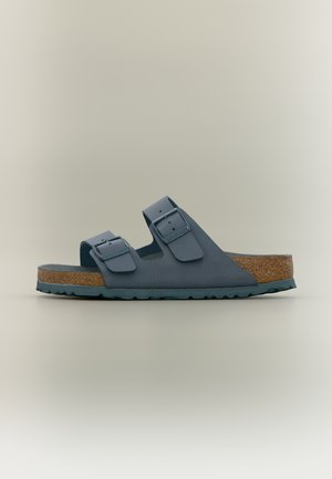 Kék, nyitott orrú szandál két állítható csattos pánttal, parafa talpbélés és texturált gumi talp, oldalról fotózva, egyszínű háttéren.