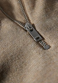 Brun stickad tyg med en slät textur, med en silverdragkedja och tänder längs placket, vilket skapar en enhetlig designaccent.