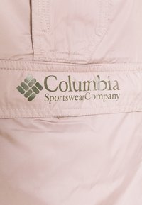 Logo de Columbia Sportswear Company sur un tissu rose clair avec des coutures visibles et un détail de poche à rabat.