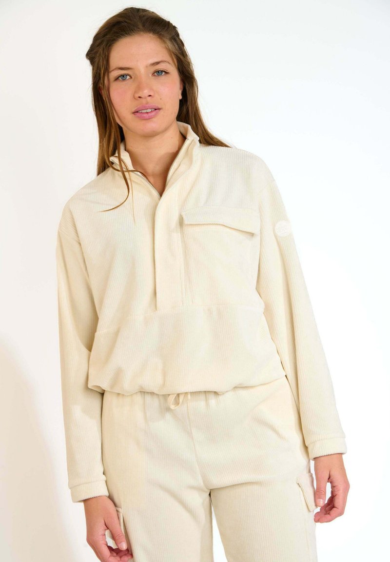 Top in corduroy beige chiaro con mezza zip, tasca sul petto e vita elastica. Tessuto testurizzato con motivo a costine. Pantaloni abbinati.