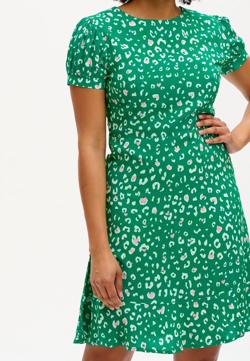 Zelené šaty s krátkými balónovými rukávy, se středně velkým leopardím vzorem v růžové a bílé barvě. Lehce průhledný materiál, přiléhavá část těla a rozšířená sukně.