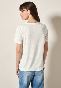 T-shirt blanc à manches courtes avec un motif texturé, encolure ronde et coupe décontractée, associé à un jean bleu clair.