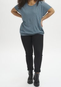 Lichtblauw gepatroneerd bovenstuk met korte mouwen, met een hexagonaal ontwerp, gecombineerd met strakke zwarte broek en zwarte enkellaarsjes.