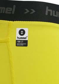 Geel prestatie-basislaag met textuurstof. Kenmerkt zich door een zwarte elastische tailleband met het "hummel"-logo en een aangehecht verzorgingslabel.