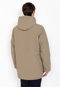 Chaqueta acolchada beige con capucha, que presenta una textura suave y detalles de costura. La parte trasera tiene un corte recto y un detalle de costura en el medio.