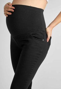 Juodos nėštumo leggingas su aukštu juosmeniu, sukurtas komfortui. Yra šoninės kišenės ir lygi, tampri medžiaga.