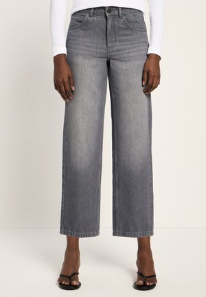 Person wearing high-waist, wide-leg grey jeans with faded front panels, paired with black open-toe heels and a white long-sleeve top.