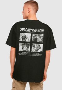 Black oversized t-shirt featuring graphics on the back, including four black-and-white images and text labeling "2PACALYPSE NOW."