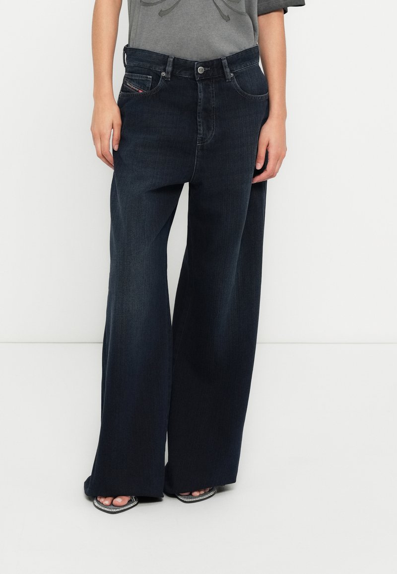 Τζιν παντελόνι με φαρδύ πόδι σε σκούρο τζην ύφασμα και ψηλή μέση, με διακριτική ξεθωριασμένη όψη, εμπρόσθιες τσέπες και κούμπωμα με ασημένιο κουμπί. Λείο υφή.