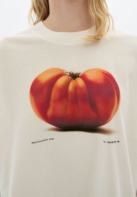Person wearing a white shirt with a large printed image of a ripe red tomato and small black text below it.