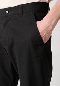 Pantaloni neri con una superficie liscia, design a gamba dritta, tasche anteriori, chiusura con bottone e cuciture a contrasto lungo le cuciture.