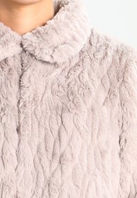 Ljusrosa fuskpälsjacka med ett texturerat vågigt mönster, med rund krage och mjukt, plyschigt tyg för ökad värme och komfort.