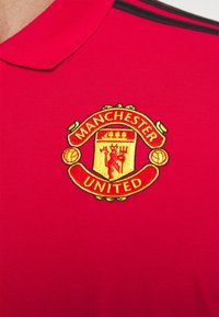Maillot de sport rouge avec le blason du club de football Manchester United brodé sur la poitrine sous le col.