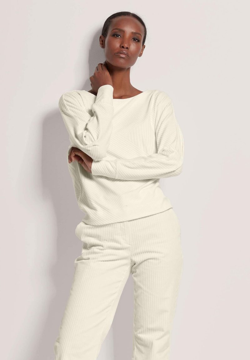 Crèmekleurige geribde trui en bijpassende broek in een gestructureerde stof, met lange mouwen en een relaxte pasvorm, tegen een effen achtergrond.