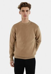 Beige geribbelde gebreide trui met een ronde halslijn en lange mouwen, voorzien van een comfortabele pasvorm en een soepele textuur.