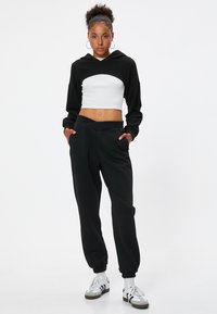 Sort cropped hoodie med buet skæring, parret med sorte joggerbukser med elastisk talje og manchetter. Hvide sneakers fuldender looket.