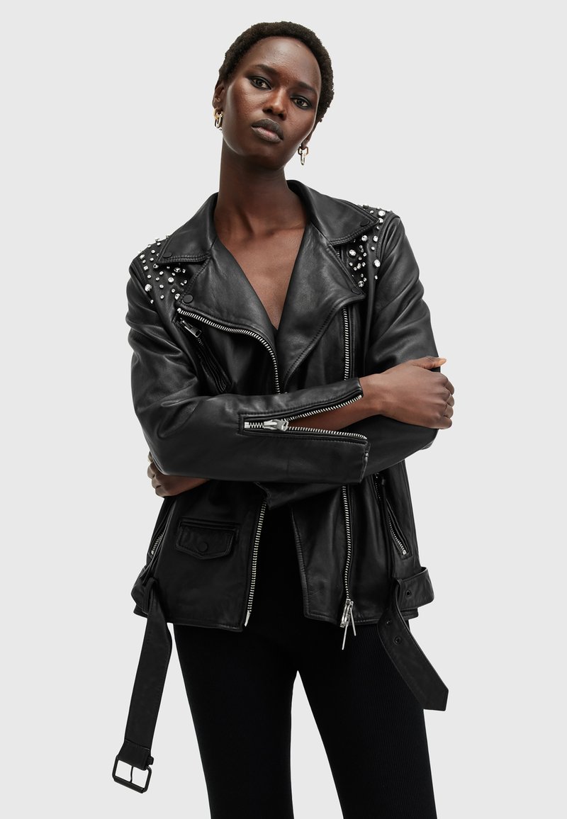 Black leather biker jacket with silver studs on shoulders, asymmetrical zippers, and a belted waist. Features a collar and side pockets.
