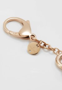 Portachiavi in oro rosa con gancio a morsetto, catena e un'etichetta circolare con incisione "SWAROVSKI" e un piccolo accento di diamante.