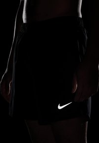 Pantalones cortos deportivos negros con cintura elástica, que cuentan con un logo de Nike blanco reflectante en el lado inferior derecho. Tejido texturizado, ajuste informal.
