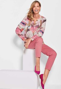 Blumenbluse mit Mustern in Pink, Lila und Beige, langen Ärmeln und Knöpfen, kombiniert mit rosa schmal geschnittenen Hosen und rosa Absätzen.