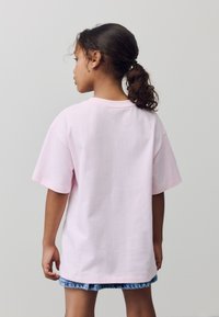 Tricou roz deschis din bumbac, cu croială lejeră, mâneci scurte și decolteu rotund, asortat cu o fustă din denim. Vedere din spate.