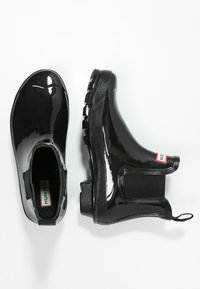 Czarne gumowe botki za kostkę z błyszczącym wykończeniem, elastycznymi panelami po bokach, teksturowaną podeszwą oraz małą metką z logo z tyłu.