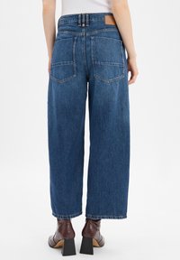 Hoge taille wijde jeans in donkerblauwe denim met een vervaagde afwerking, voorzien van twee achterzakken en een leren merkpatch op de taille.