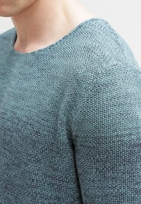Maglione lavorato a maglia in tonalità blu gradienti, caratterizzato da un tessuto testurizzato, ampio scollo e dettagli a coste sulle spalle e sul colletto.