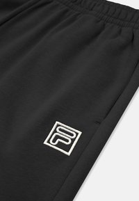Tessuto di felpa nera con cintura elastica, con un logo ricamato bianco sul lato sinistro. Texture morbida con vestibilità rilassata.