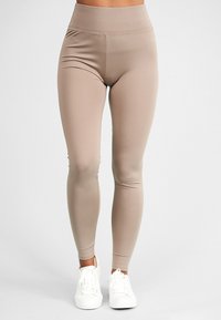 Høytlivs tights i et lyst brunt, elastisk stoff med en glatt tekstur, med en tettsittende fasong og konturdetaljer. Kombinert med hvite joggesko.