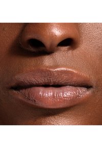 Nærbilde av glatte lepper i en nudeskygge, med subtile glans, teksturert hud og et naturlig utseende mot mørkere hudtoner.