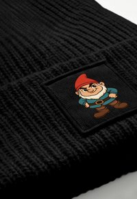 Black knit beanie featuring a square patch with a cartoon gnome in a red hat, blue shirt, and brown pants. Textured fabric.