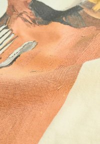 Textiel met een roze en beige ontwerp en een gestructureerd oppervlak. De visual bevat ruwe elementen en duidelijke patronen in het materiaal.