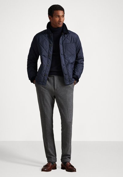 Jūras zilas quiltētas jakas ar pogu aizdari, izteiksmīgu apkakli un krūšu kabatu. Apvienota ar teksturētām pelēkām biksēm un brūnām oficiālām kurpēm.